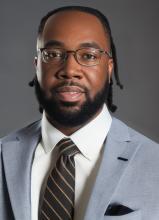man in a grey suit with glasses on smiling lightly