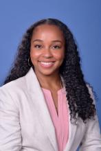woman in a blazer with dark curly hair smiling