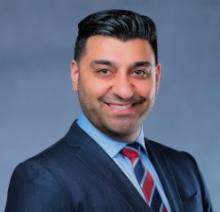 man with his hair slicked back in a suit smiling