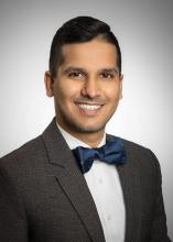 man in a grey suit with a dark blue bowtie on smiling