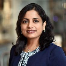 woman with dark hair, in a navy blue blazer smiling