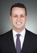 man with dark brown hair in a suit smiling