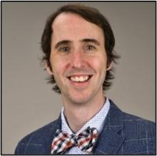 Man smiling while wearing a bow tie in front of a grey background