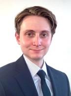 man with dark blonde hair, in a blue suit smiling lightly