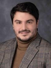 man in a brown turtleneck and plaid blazer smiling