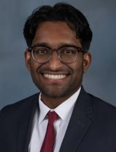 man with his hair in a middle part and glasses on smiling