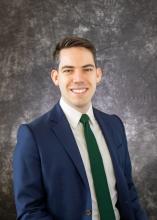 man in a blue suit, with dark hair smiling