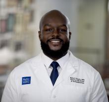 bald man with a dark beard in a white doctor coat smiling