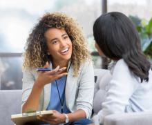 A doctor with curly dark hair with blonde highlights smiling at another person she's speaking with