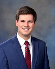 man in a blue suit with dark brown hair smiling