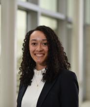 woman with curly hair in a black blzer and white top smiling