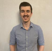 man with brown hair in a blue plaid button down, smiling