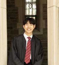 man in a red tie and black graduation gown smiling