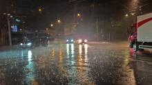 A photo taken at night of an intersection with cars driving through the rain. 