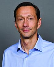 man with brown hair and a blue button down on, smiling