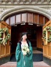 woman in green graduation robes holding flowers