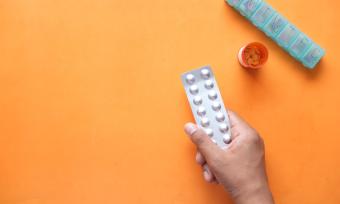 Hand holding white pills on an orange background
