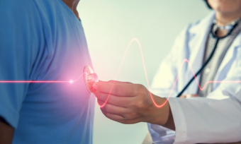 Doctor using a stethoscope to listen to patient's heart, graphic of heart beat displayed over image with red line. 