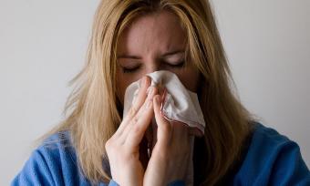 Blonde woman sneezing into a tissue
