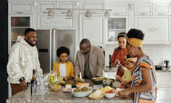 Photo of a family surrounding a kitchen island covered in food. 