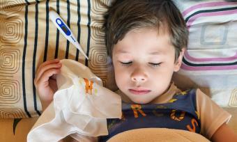 Photo of a little boy in bed with a thermometer and a hankerchief  