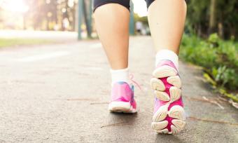 Close up photo of feet wearing tennis shoes, walking on a sidewalk.