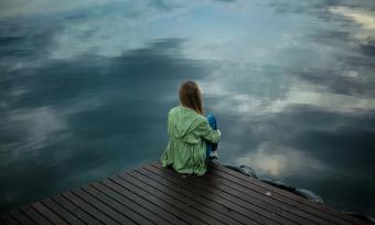 Photo of a woman sitting alone on a dock in the dim fall light. 