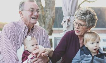 A photo of an elderly couple holding their young grandchildren