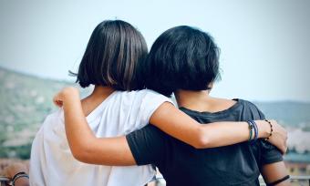 A photo taken from behind of two girls hugging, supporting each other during a difficult time. 