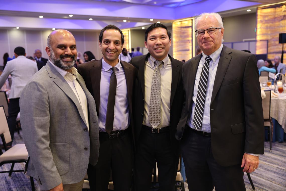 4 men standing together, dressed in suits, smiling