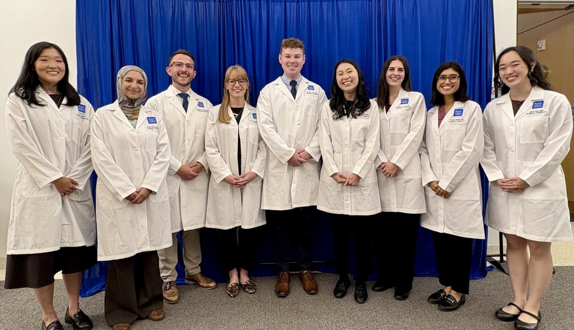 Nine students in white coats lined up, smiling