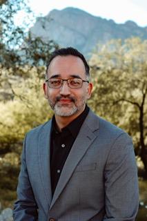 man with glasses on smiling in front of nature background