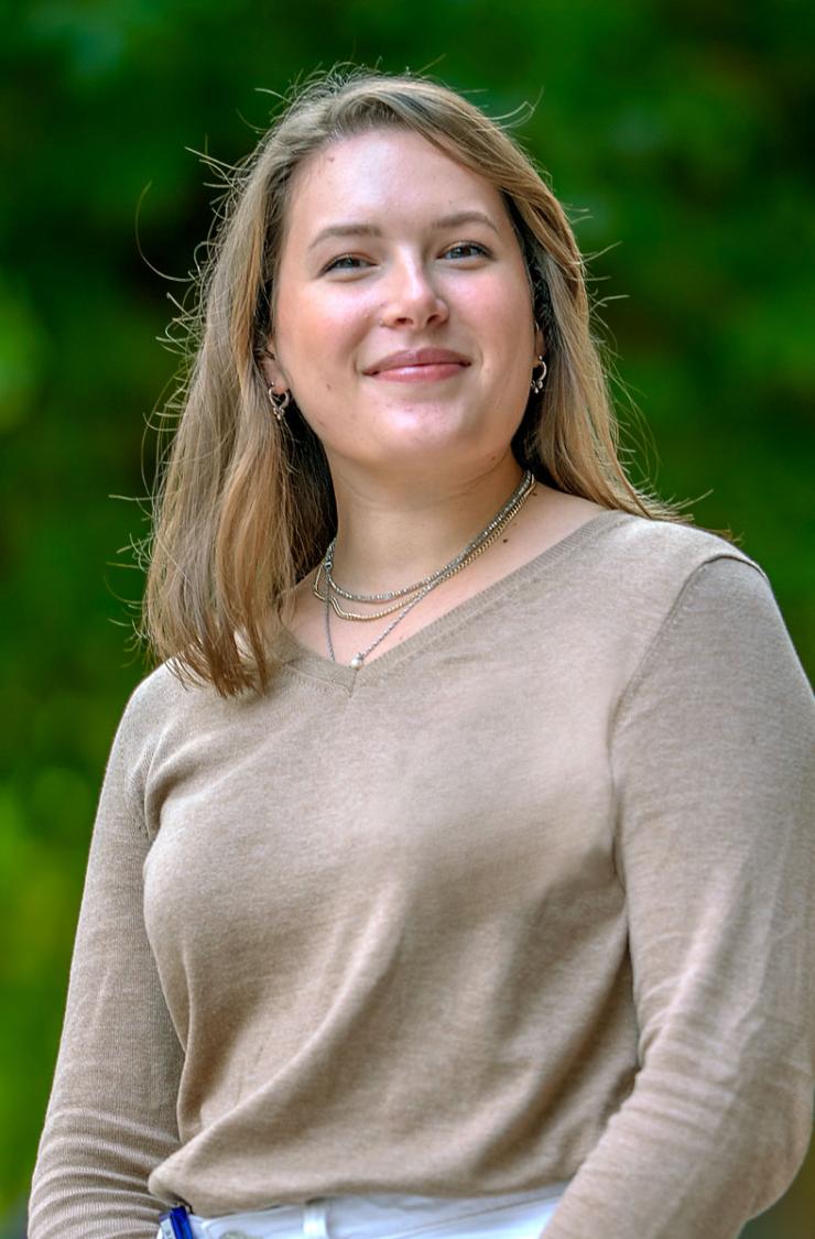 Person with shoulder-length hair and layered necklaces, standing outdoors