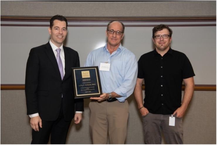 3 people standing together smiling, with one holding an award