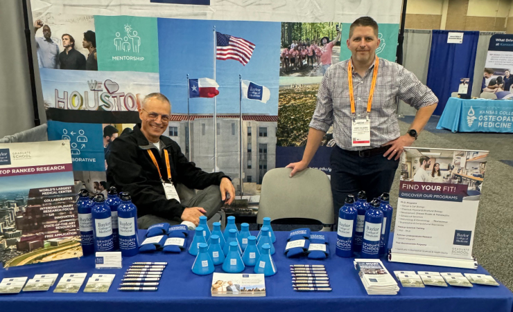 Two people standing at a booth decked with Baylor tchotchkes during a recruiting event.