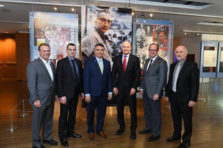 Dr. Robert Britton, Dr. Marco Sardiello, Dr. Adam Kuspa, Dr. Christie Ballantyne, Dr. Carl Allen and Dr. Aleksandar Milosavljevic stand in front of a photo of Dr. Michael E. DeBakey.
