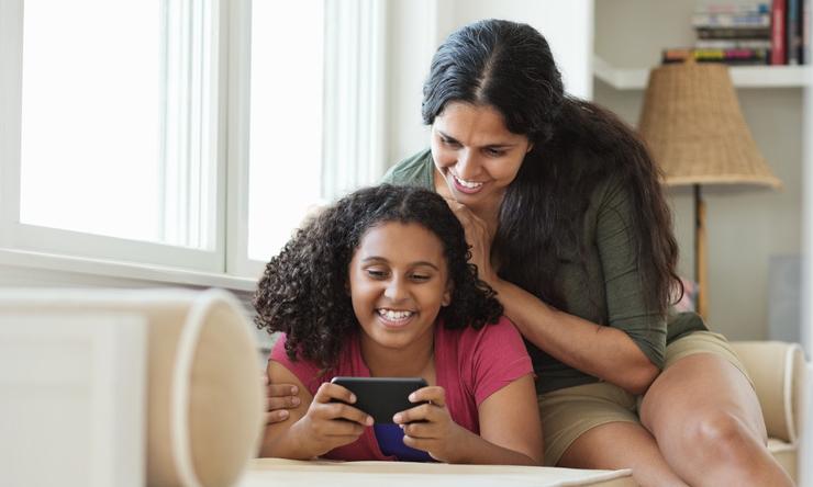 A mother and daughter relaxing together while looking at something on a smartphone.