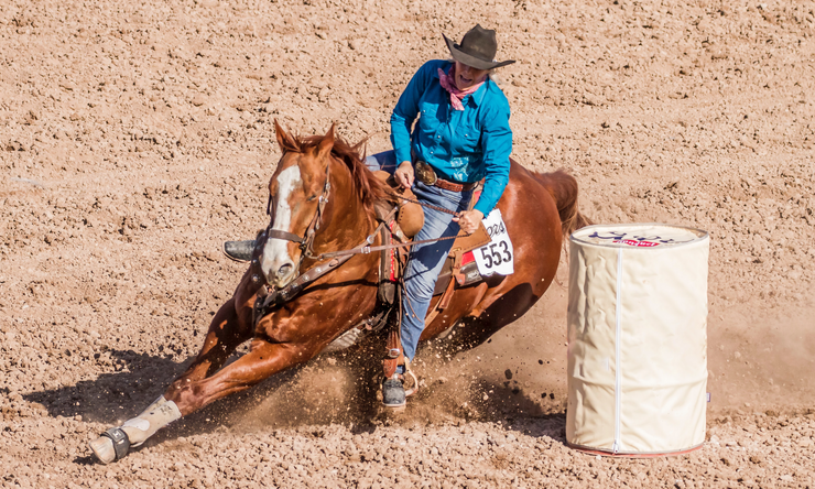 A person riding on a horse in a race, taking a hard turn around a barrel.
