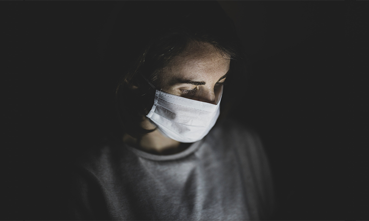 A person wearing a face mask reading information on a laptop.