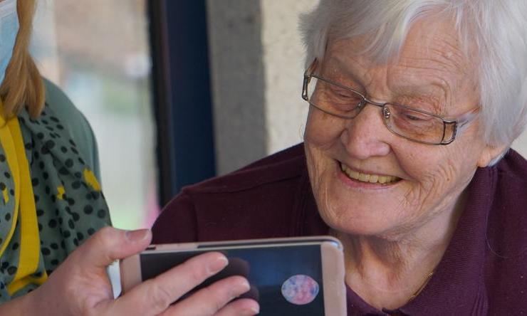 A mother watching Mother's Day messages from family on a phone with help from an adult in a face mask.