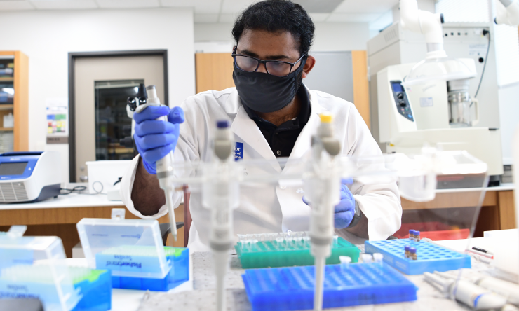 A researcher wearing a face mask works in a lab.