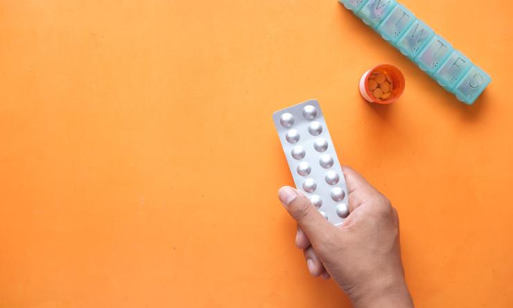 Hand holding white pills on an orange background
