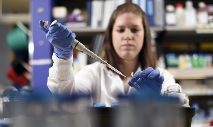 Woman using a pipette as viewed through a laboratory shelf