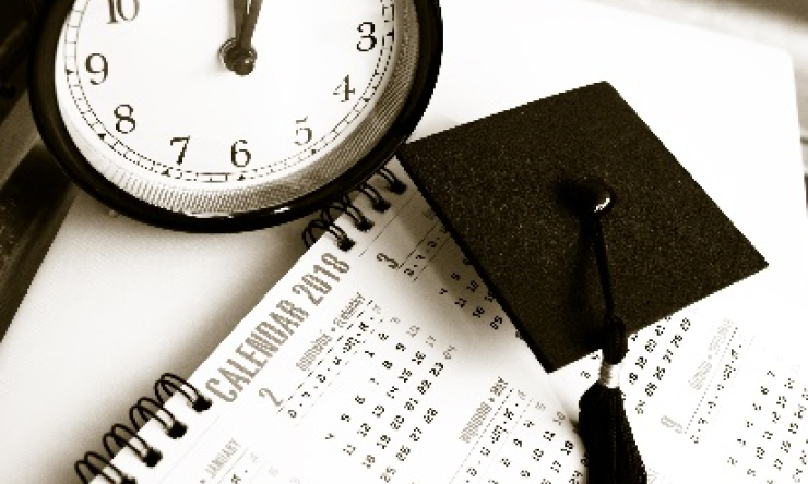 A clock and graduation cap sitting on top of a calendar page.