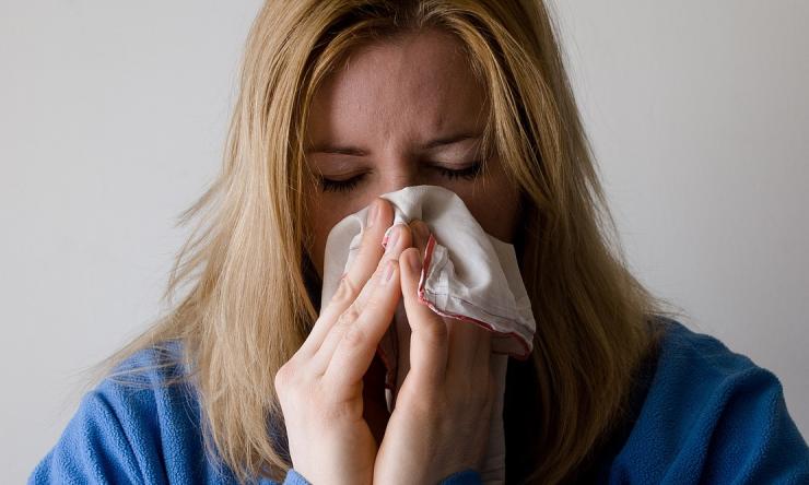 Blonde woman sneezing into a tissue