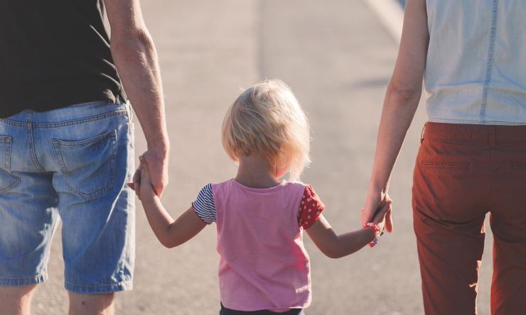 Photo taken from behind of a child holding the hands of their parents. 