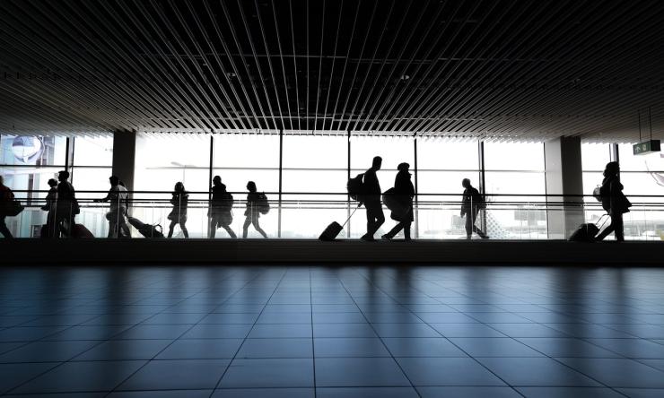 Photo of people in silhouette walking in front of a window at the airport. 