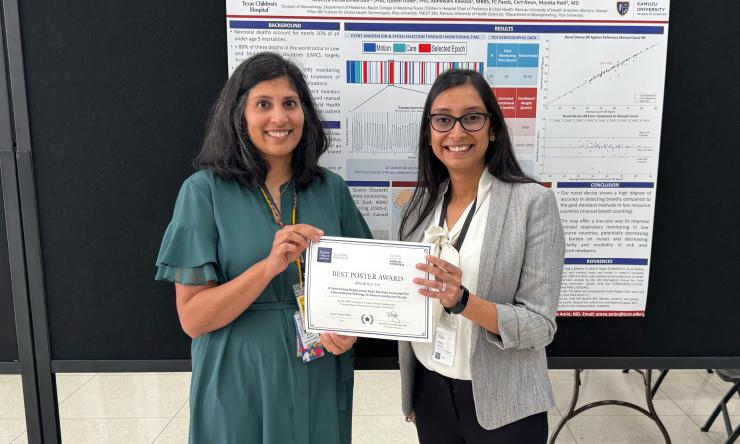 two woman standing in front of poster, holding an award certificate