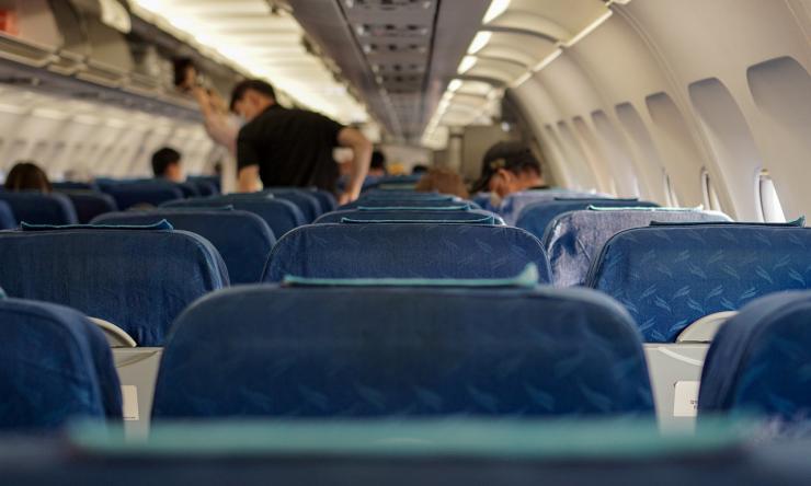 Photo of empty seats on an airplane with travelers blurred in the background. 