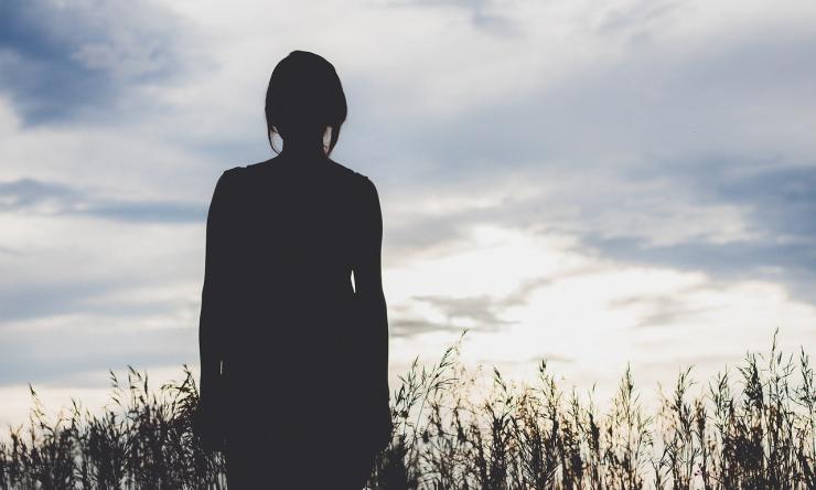 Silhouette of female standing in front of tall grass.